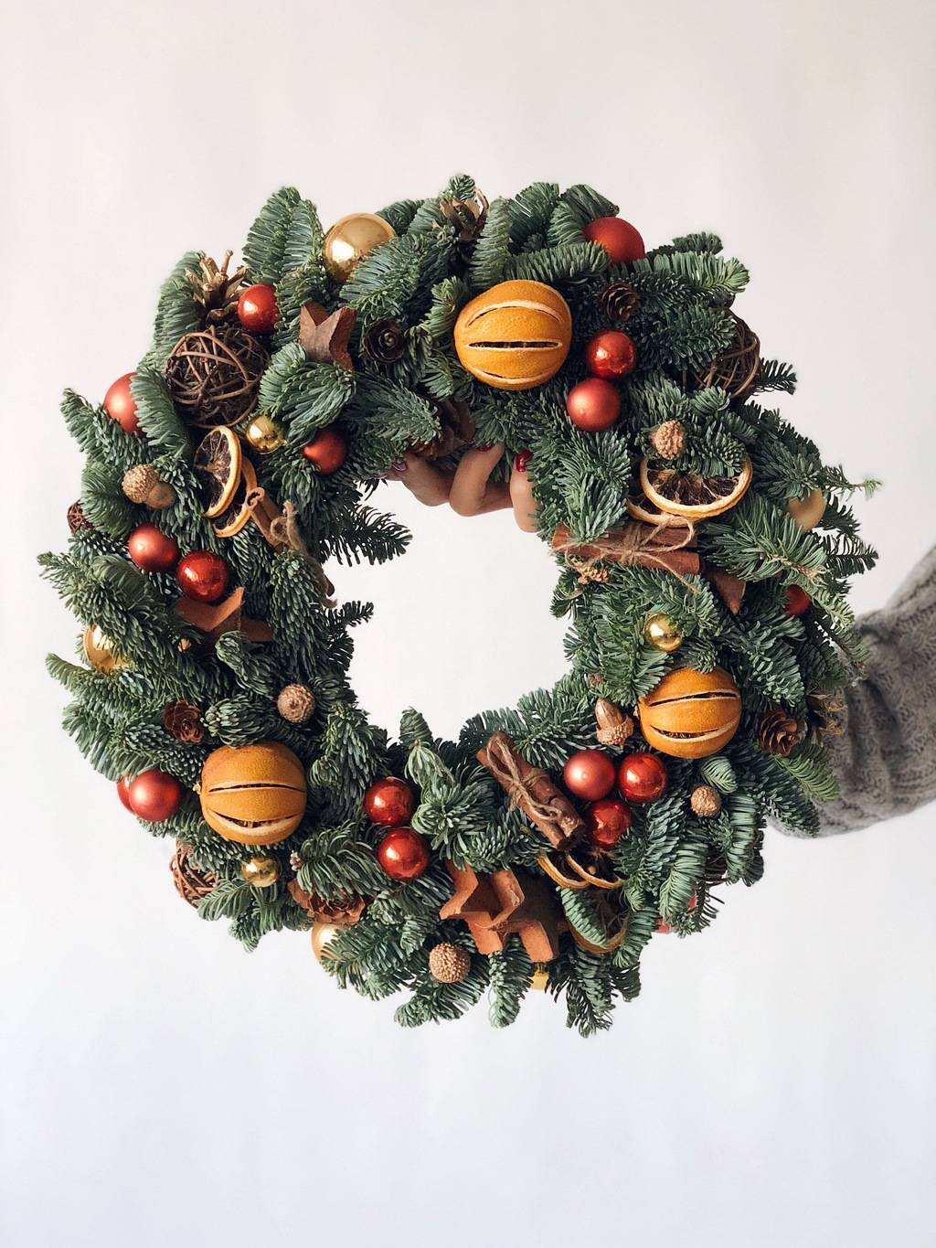 white background woman holding christmas wreath decorated with dried fruits 