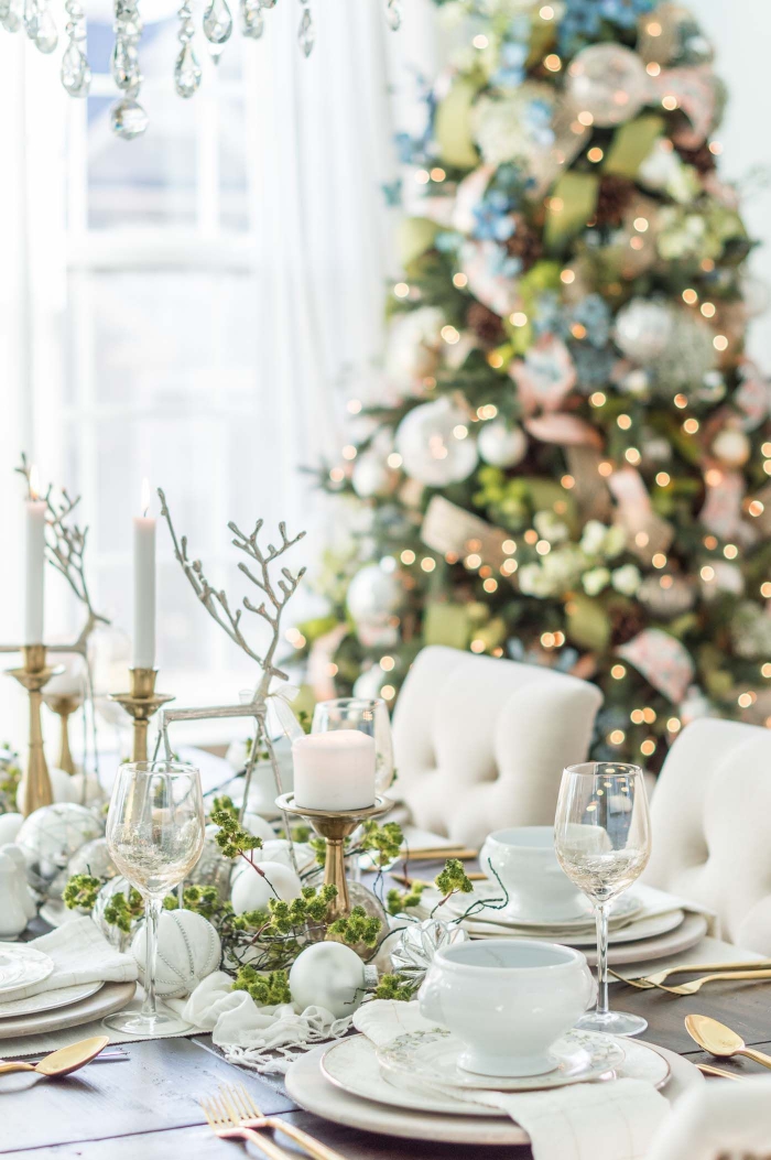 table decorated with natural christmas decorations in white golden and green christmas tree in the background