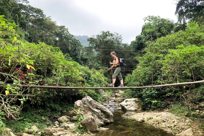 Woman crossing a bridge over a river trekking jungle