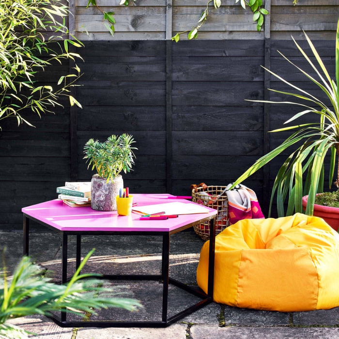 Patio area with bright statement furniture pink side table and bright yellow puff