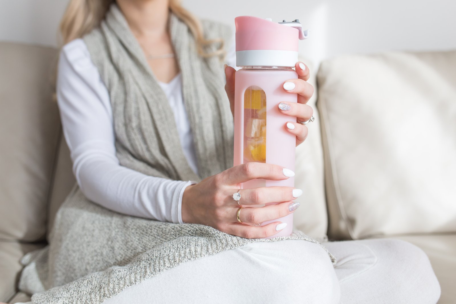 woman sitting on a couch holding pink pressa water bottle 