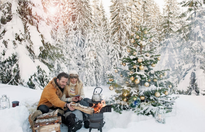 Couple in snowy forest campfire making tea decorated christmas tree 