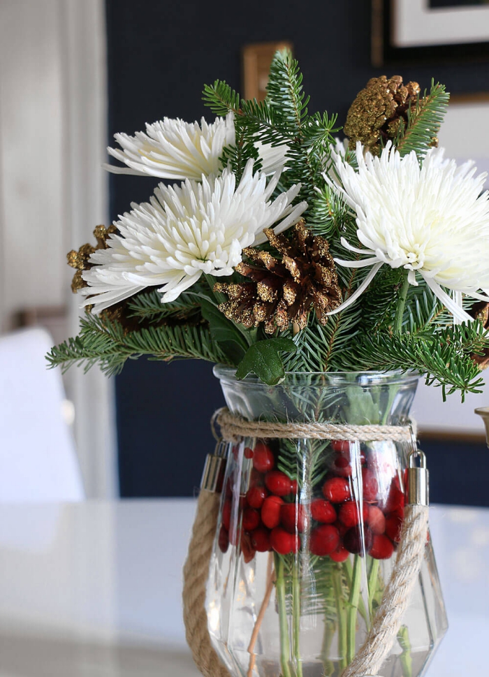 Close up christmas flower arrangement with gold spray painted pinecones white flowers green branches and berries