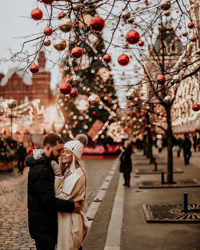 couple cuddling in front of large christmas tree red and gold baubles city festive season
