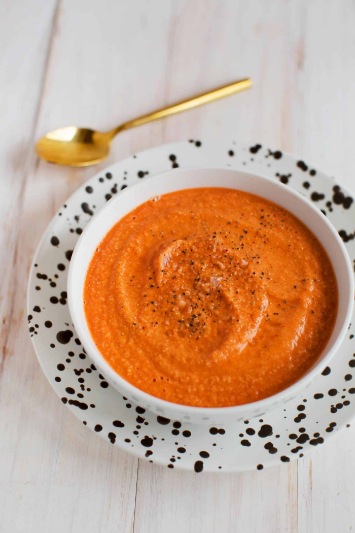 Low Carb Dinners creamy tomato soup in a white bowl with black and white plate golden spoon