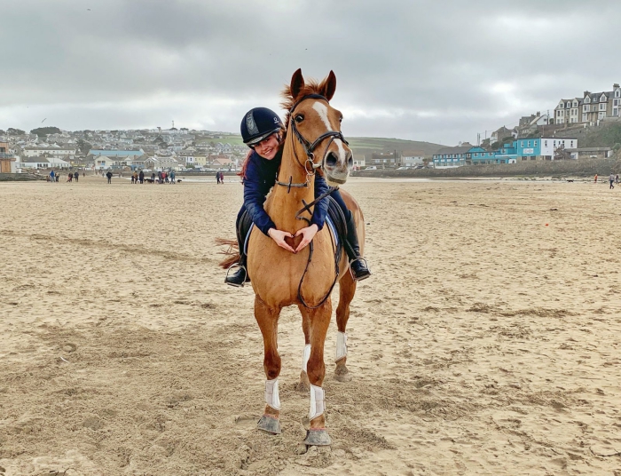 Woman riding a horse on a beach forming heart with her hands