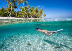 Woman swimming underwater in clear tropical waters in front of exotic island
