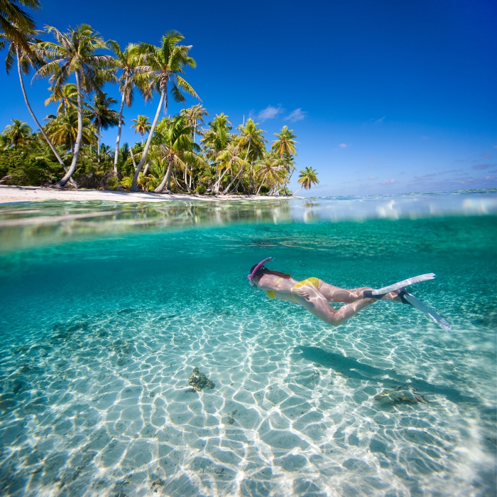 Woman swimming underwater in clear tropical waters in front of exotic island