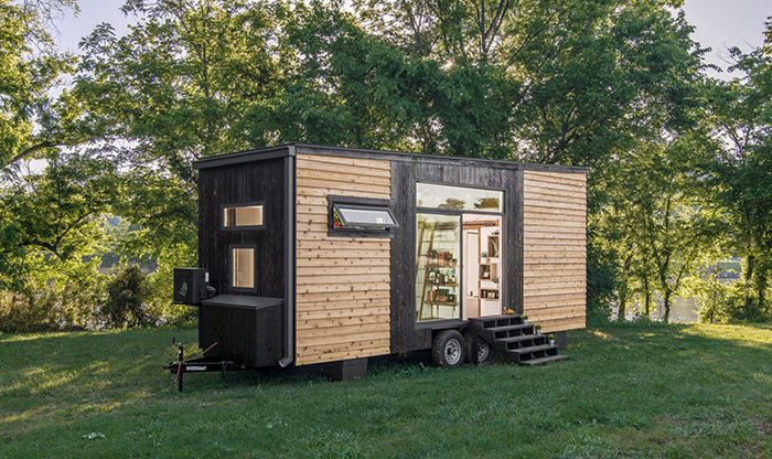 Modern wooden tiny house on wheels on a green lawn trees