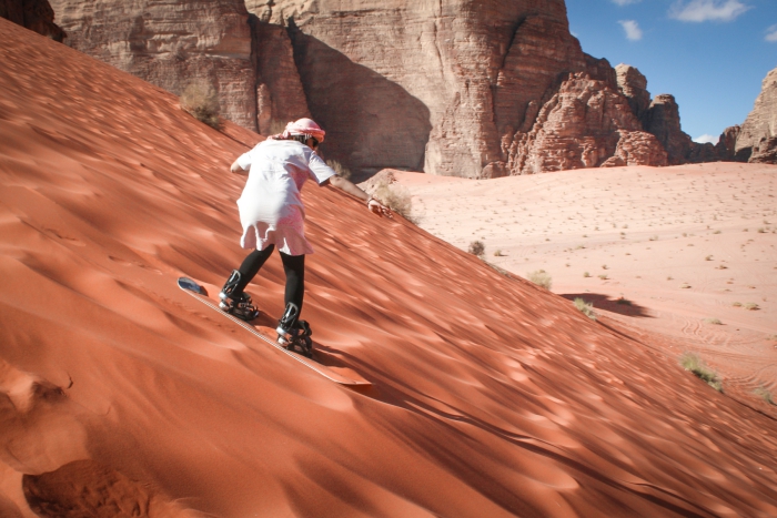 Man with shemagh sliding down a dune in the desert 