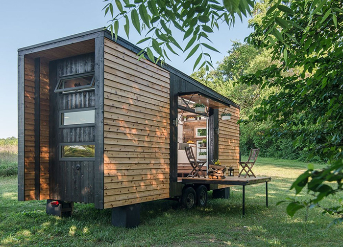 Best Cozy Tiny Homes wooden home on wheels with a small balcony in a field