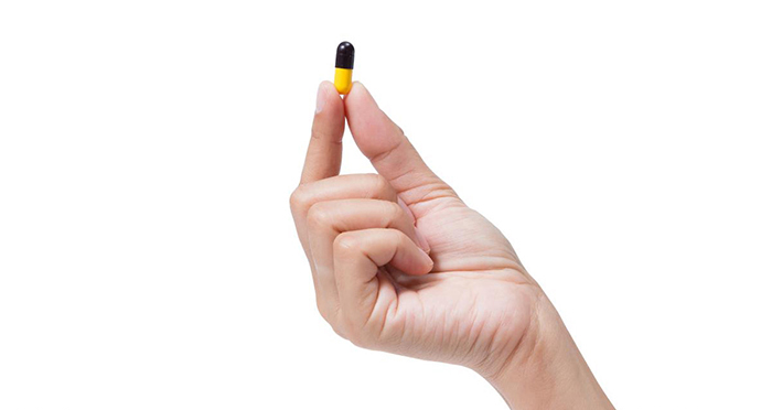 hand holding a yellow and black capsule of antibiotics