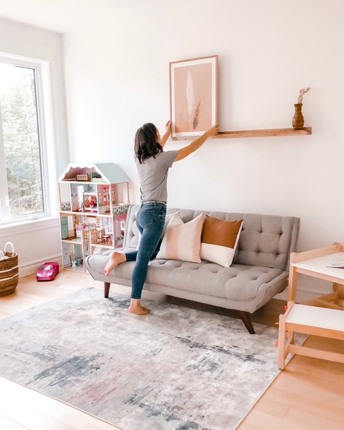 woman hanging a picture on a shelf living room design idea 