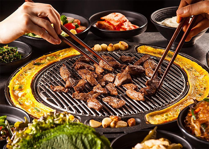 Korean Cuisine Barbecue tow people eating with chopsticks grilled pieces of meat 