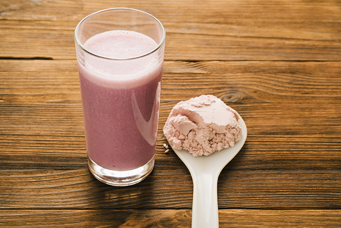 Protein powder in a spoon next to a glass full of pink shake