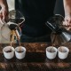 a man pours two-cup specialty coffee into four transparent coffee cups