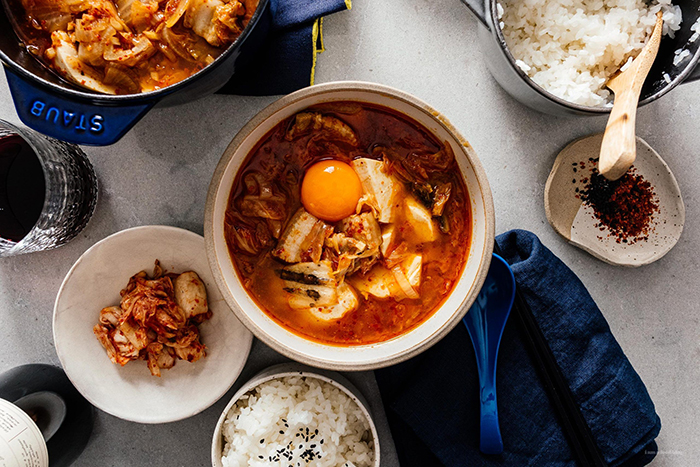 Korean soft tofu stew on a table with an egg rice bowls spices