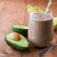 Chocolate protein in a glass with a straw next to banana and avocado