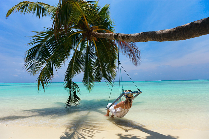 Exotic places woman in a hammock on a palm tree the Maldives clear blue water