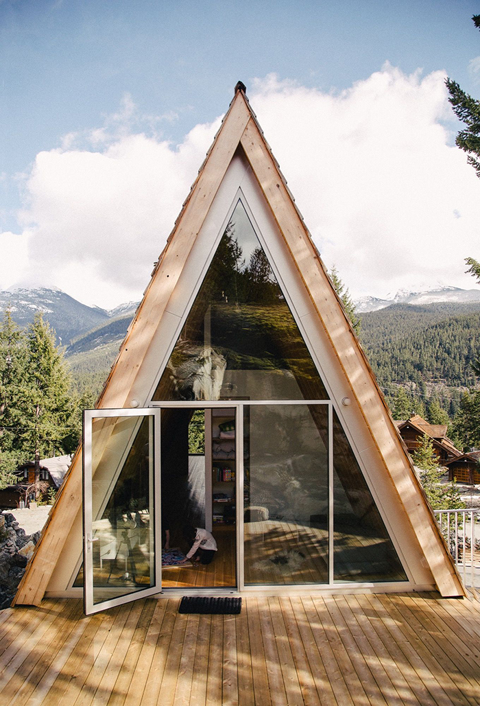 Prefabricated mountain bungalow in the woods with a large glass window and a front porch