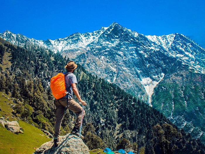 hiking during the summer a man with an orange backpack in the mountain looking at a peak covered with snow