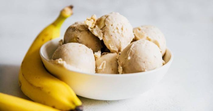 two bananas on a table with a cup full with banana ice cream balls