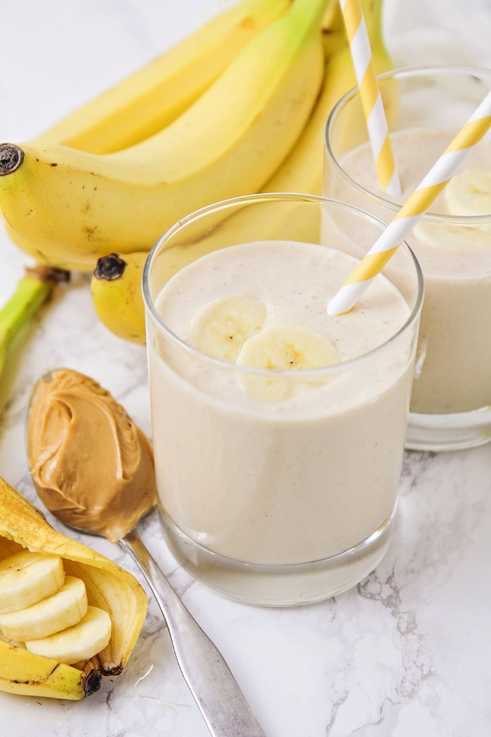 banana smoothie in a glass with a straw and bananas in the background spoon of peanut butter