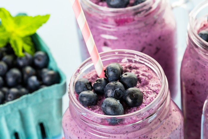berrie spinach smoothie in jar with a straw and blueberries