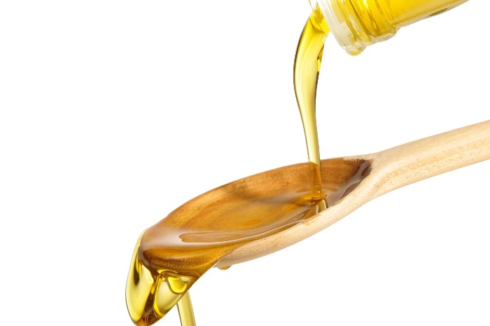 carrot seed oil pouring on a wooden spoon from a glass bottle