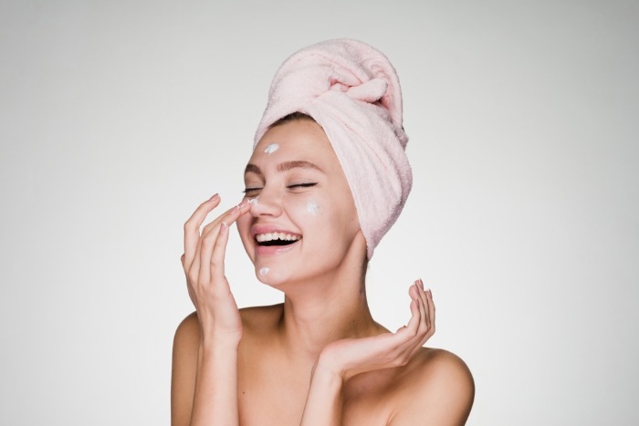 woman with a towel on her hair smiling and applying face cream