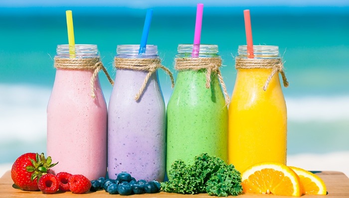 cooling smoothies four bright coloured smoothies with fruits in front with the sea in the background