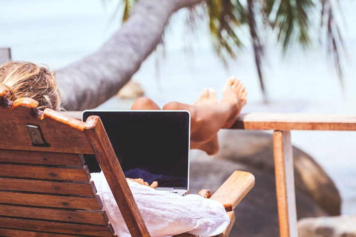 digital nomads woman lying with a computer on beach with palm trees