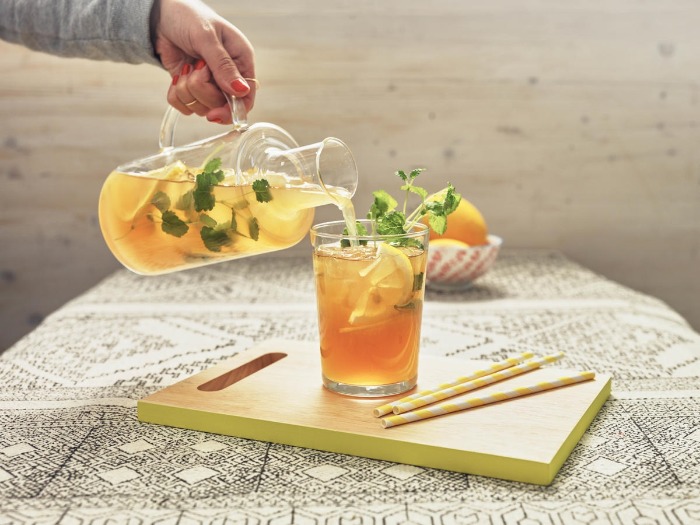 person pouring ginger ice tea with herbs in a glass on a table