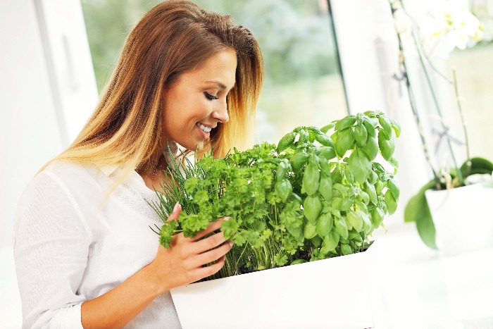 woman dressed in white bending over a pot of herbs smiling