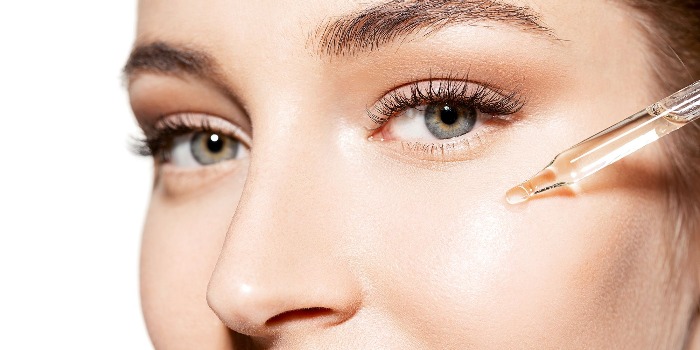 woman with light eyes applying hyaluronic acid on her cheeks close up