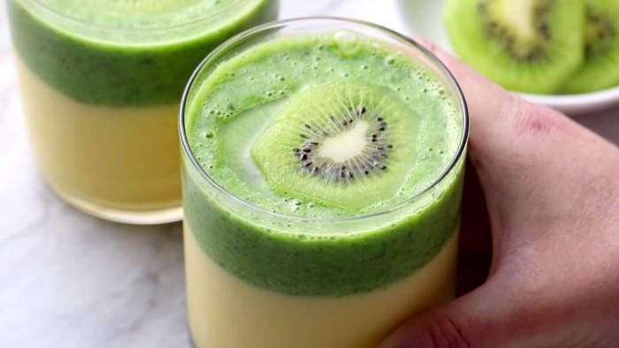 two color cooling kiwi smoothie in a glass with a piece of kiwi inside