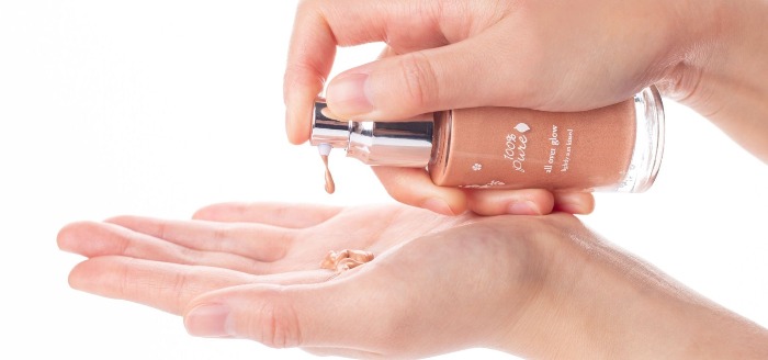 Two hands holding a liquid bronzer and using drops in a palm