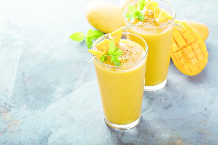 two bright yellow mango smoothies on a stone table top