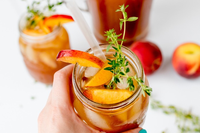 peach ice tea with thyme in a jar with pieces of peach and a straw
