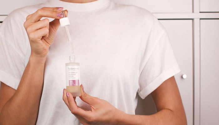 woman with white shirt testing and using hyaluronic acid holding a bottle