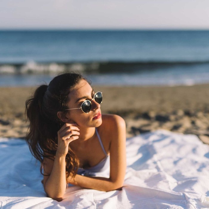 girl with black sunglasses lying on the beach looking at the sun
