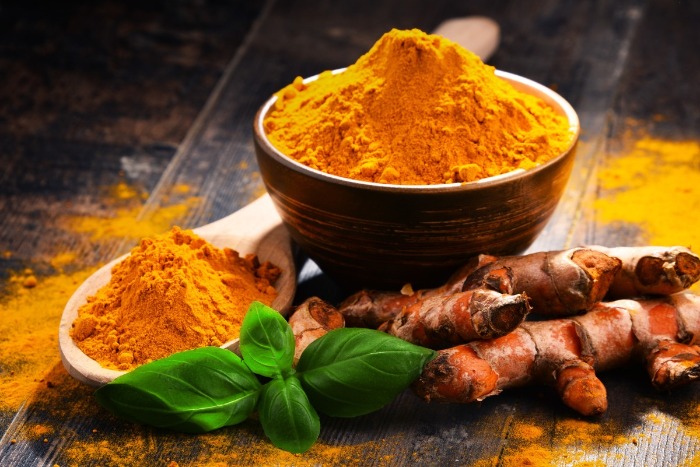 a bowl and wooden spoon full of turmeric on a table top turmeric roots