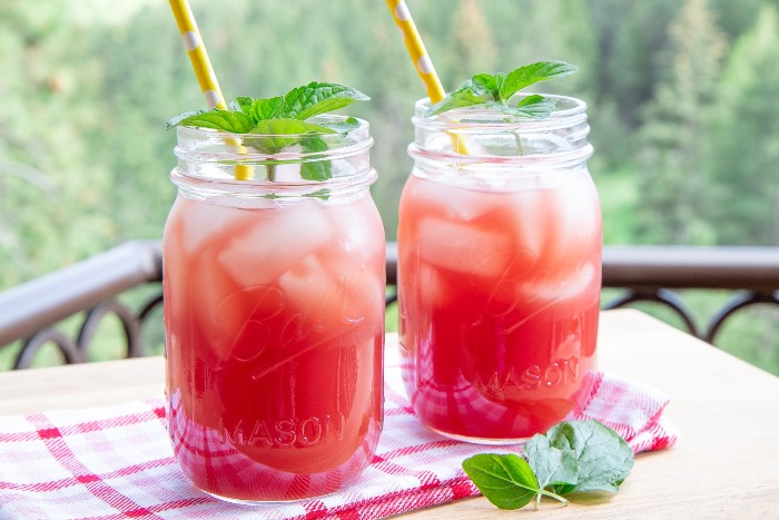 two jars with red watermelon iced tea outdoors with yellow straws