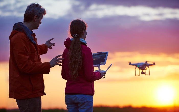 father teaching daughter how to fly a drone shooting sunset