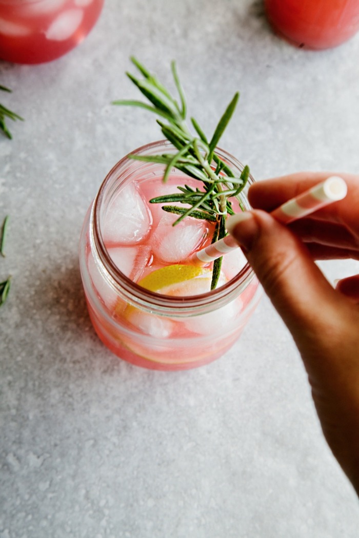 hand stirring a rosemary cocktail with a straw 