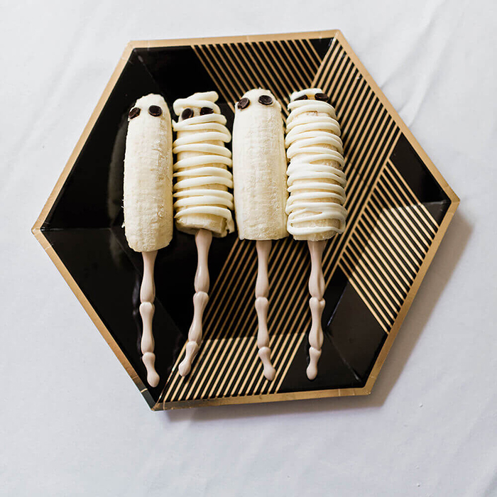 Banana mummies on skeleton sticks in a black and gold plate chocolate chip eyes