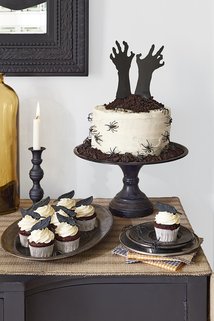 Halloween cakes ideas white cake with hands sticking out and spiders on a table with muffins and a candle 