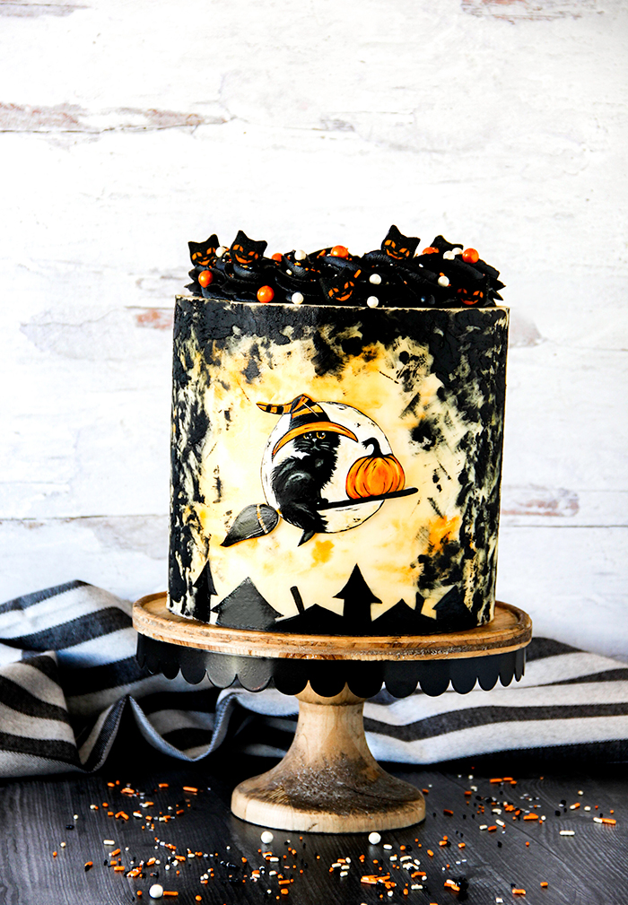 Cat and witch cake with black cats on top and a black cat on a broom on a wooden stand