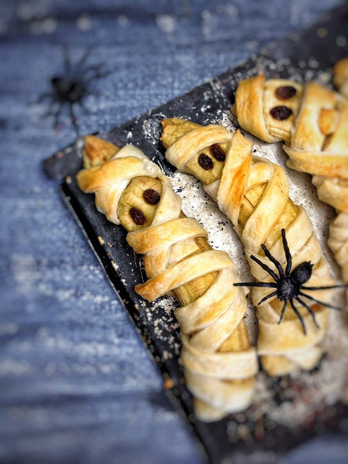 Halloween treats banana mummies with spiders on black table baked bananas