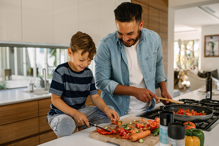 new hobbies a man and a boy cooking together at home chopping vegetables and smiling